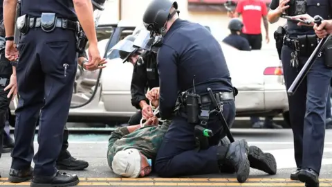 Getty Images A man is arrested by Los Angeles police officers for violating curfew in Hollywood