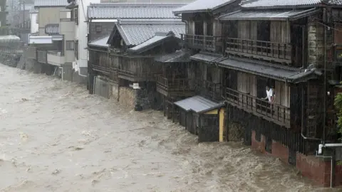 Reuters Men watch from their balcony as a river floods their home in Ise