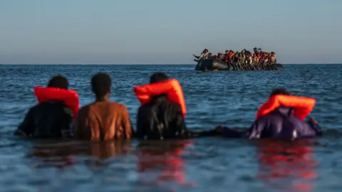Migrants wait in the sea to try and board a dinghy to cross the English Channel on August 25, 2025 in Gravelines, France. 