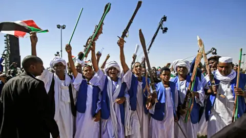 AFP Supporters of Sudan"s President Omar al-Bashir raise up sticks and swords in salute as they gather during a rally for him in the Green Square in the capital Khartoum on January 9, 2019