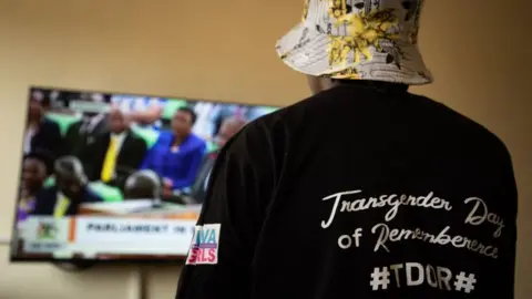 AFP A Ugandan transgender woman who was recently attacked and currently being sheltered watches a TV screen showing the live broadcast of the session from the Parliament for the anti-gay bill, at a local charity supporting the LGBTQ Community near Kampala on March 21, 2023.