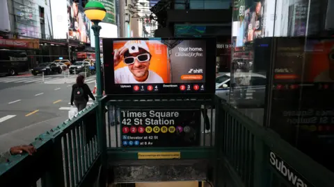 Shift An advert for Shift showing a young man wearing a white T-shirt, glasses and cap with a camera on the visor, and the words "Your home. Cleaned for free." above a subway entrance to Times Square 42 St Station