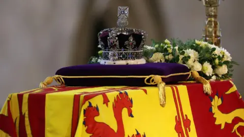 PA Media The coffin of Queen Elizabeth II, draped in the Royal Standard with the Imperial State Crown and the Sovereign's orb and sceptre, lying in state on the catafalque in Westminster Hall, at the Palace of Westminster, London. Picture date: Wednesday September 14, 2022.