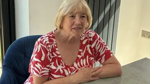 Lea, who has blonde hair in a bob and is wearing a red and white patterned top.