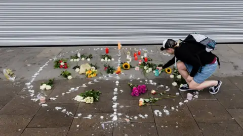 Getty Images A woman places a candle at a makeshift memorial arranged like a peace sign at the scene of a knife attack in the northern German city of Hamburg, 29 July 2017