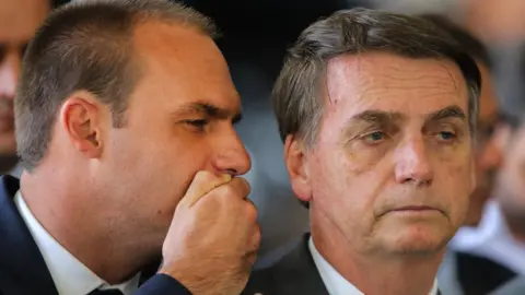 Getty Images Eduardo whispering to his father, Jair Bolsonaro, at a conference in November