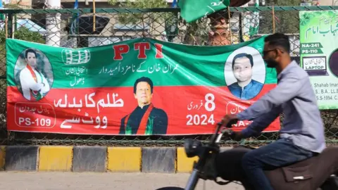 EPA People drive past electoral posters of jailed former Prime Minister Imran Khan