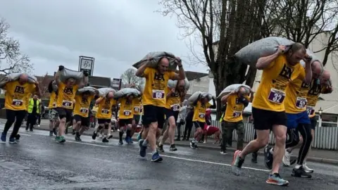 BBC/Olivia Richwald Runners in yellow t-shirts carry sacks of coal on their backs