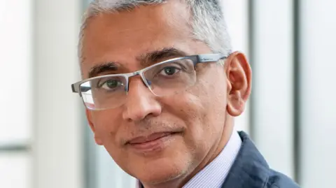 University Hospital Southampton Prof Salim Khakoo looks at the camera. He has light grey hair and glasses and is wearing a jacket and smart shirt.