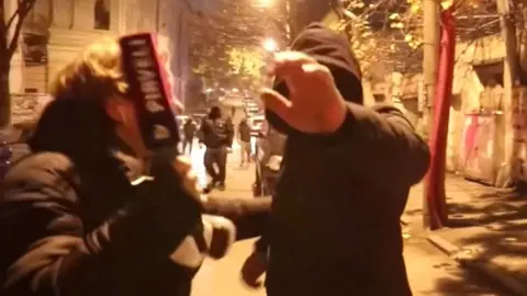 Journalist being approached by a masked man with his hand up