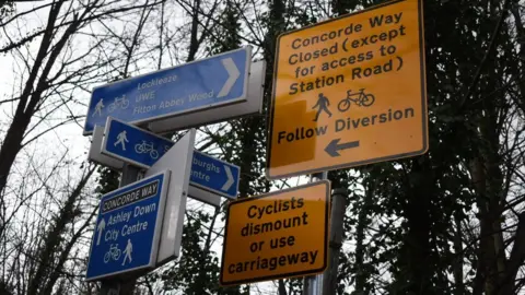 Alex Seabrook/LDRS Sign posts advising cyclists to get off and walk or ride down the busy Muller Road