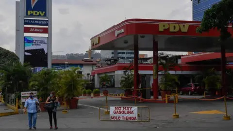 AFP People walk past a closed petrol station in Caracas, Venezuela (14 May 2020)