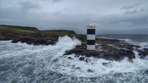 Douglas Cecil Waves crashing against the rocks near a small lighthouse on Rathlin Island