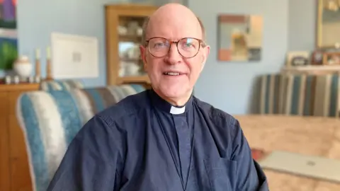 Alex Dunlop/BBC Martin Seeley, the Bishop of St Edmundsbury and Ipswich, sitting in his home