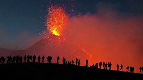 Hikers watch as Mount Etna erupts against the night sky