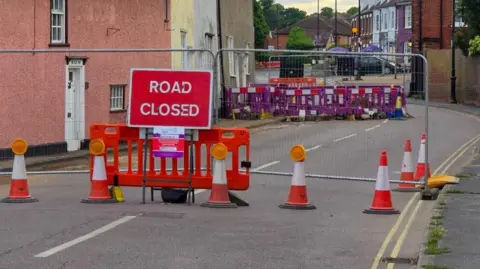 A photo showing a Road Closed sign, traffic cones and metal fencing cordoning off part of Station Road