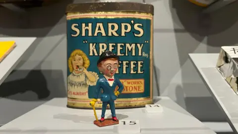A miniature tin figure of Sir Kreemy Knut, wearing a blue suit with monocle and walking cane, on display in The Oldham Gallery at Maidstone Museum
