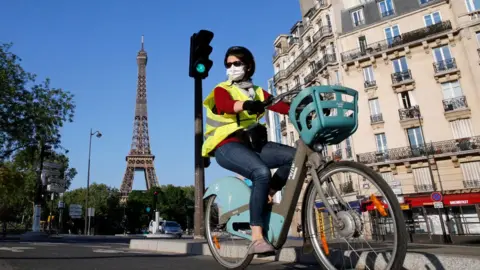 Getty Images A woman wearing a face mask rides her bicycle in Paris, with the Eiffel Tower captured behind her