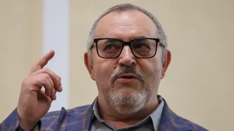 Boris Nadezhdin, who has short grey hair, wears a colourful blazer and glasses in court in Dolgoprudny, Moscow region, last month. He is pointing upwards with his right index finger.