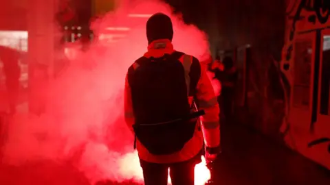 Reuters A French SNCF railway worker on strike holds a flare as he walks through Gare du Nord railway station before a demonstration against the French government's pension reform plans in Paris as part of a day of national strike and protests in France, 5 December, 2019.