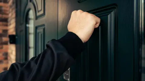 A close up of a fist knocking on a black door. 