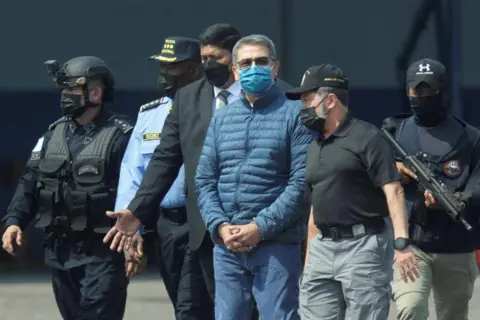 Reuters Honduras former President Juan Orlando Hernandez is escorted by authorities as he walks towards a plane of the U.S. Drug Enforcement Administration (DEA) for his extradition to the United States