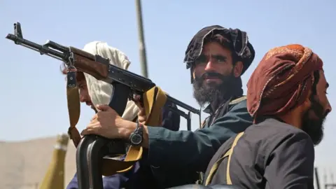 Getty Images Taliban fighters stand guard in a vehicle along the roadside in Kabul on 16 August.