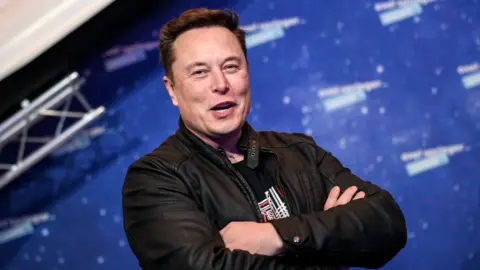 Getty Images Elon Musk laughs with arms folded in this file photo