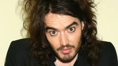 Getty Images Portrait of Russell Brand looking at the camera. He has facial hair and long hair