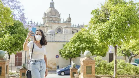 Getty Images A woman wearing an N95 mask poses for a selfie next to a tourist attraction in Spain