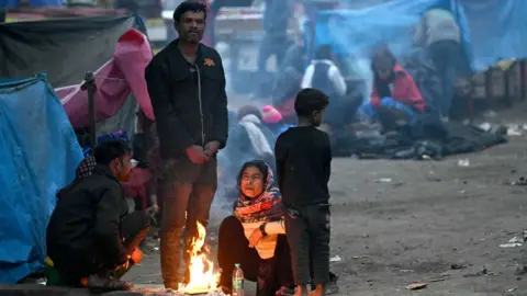 Getty Images People sit next to a bonfire to keep themselves warm during a cold winter morning in New Delhi on January 2, 2024. (Photo by Money SHARMA / AFP) (Photo by MONEY SHARMA/AFP via Getty Images)