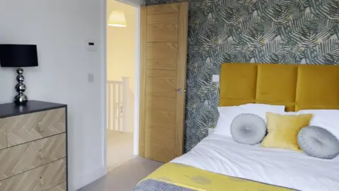 A bedroom at Bridge View with a yellow bedhead and patterned wallpaper