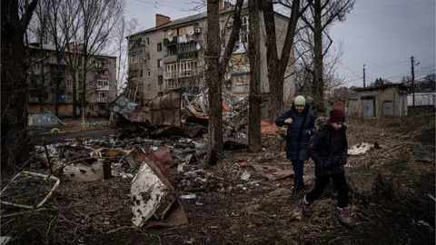 Getty Images A woman and her son walk by a residential building that was heavily damaged in recent attacks by the Russian forces in Kostiantynivka, Ukraine on February 27, 2023