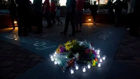 Getty Images Candles wrap around a collection of flowers laid at the memorial