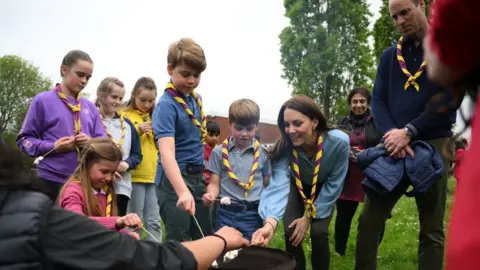 Getty Images Britain's Prince William, Prince of Wales (R) looks on as (L-R) Britain's Princess Charlotte of Wales, Britain's Prince George of Wales, Britain's Prince Louis of Wales and Britain's Catherine, Princess of Wales toast marshmallows as they take part in the Big Help Out, during a visit to the 3rd Upton Scouts Hut in Slough, west of London