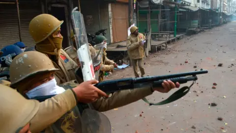 Getty Images A police personnel aims his gun towards protesters during demonstrations against India's new citizenship law in Kanpur on December 21, 2019.