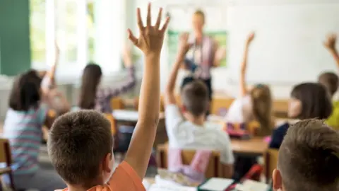 Getty Images/Skynesher Schoolboy raising hand to answer question in class