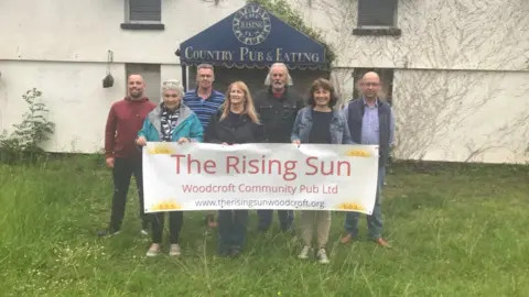 The Rising Sun Pub Campaigners stood outside The Rising Sun in Woodcroft holding a banner