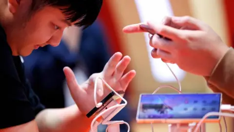 AP Man preparing to touch a small screen with his left forefinger. Wires and a larger screen, and another pair of hands,  can also be seen. 