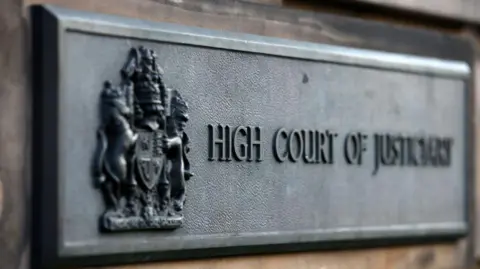 A metal sign reading High Court of Justiciary attached to a wall outside the High Court in Edinburgh
