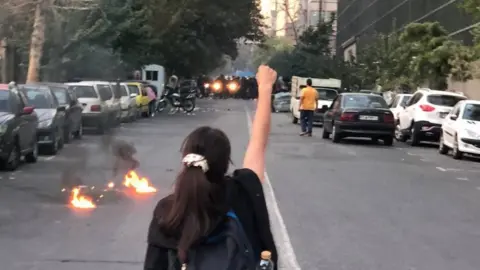 A young woman without a headscarf raises a fist at a protest in Iran sparked by the death of Mahsa Amini