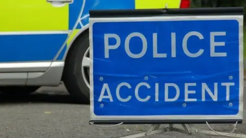 Cambridgeshire Police A police sign which says 'police accident' placed in front of a police car on the road.