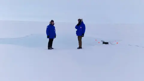 Real Ice Two researchers are wrapped up in Arctic gear as they watch the seawater pump in action