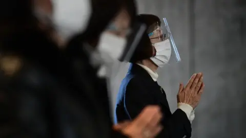 Getty Images A worshipper wearing a plastic visor and face mask prays during Christmas Day Mass at St. Mary's Cathedral on December 25, 2020 in Tokyo, Japan.