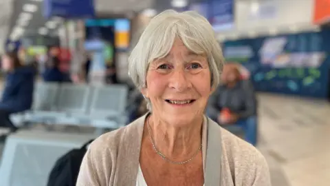 Grey haired lady smiling wearing a beige cardigan 