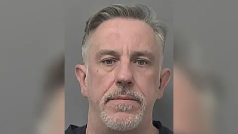 A police head and shoulder's photo of David Young, who has short grey hair and a short grey moustache and beard. He is looking into the camera with a serious expression.