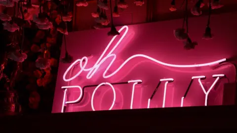 Getty Images A pink fluorescent sign of the Oh Polly logo against a black backdrop.