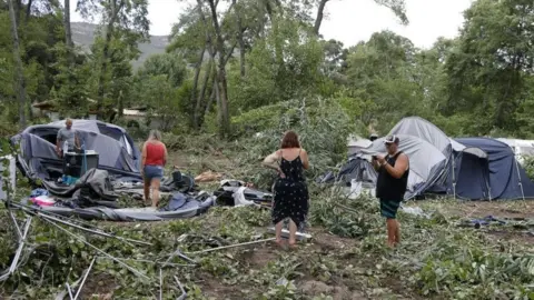 Getty Images Campers stand among tents destroyed by wind and fallen foliage.