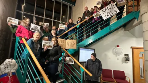 Chas Townley A group of people standing on the stairs holding signs asking for trees to be saved