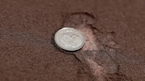 EPA View of a coin next to the ash from the Sangay volcano on a street in Alausi, in the province of Chimborazo, Ecuador, 20 September 2020.